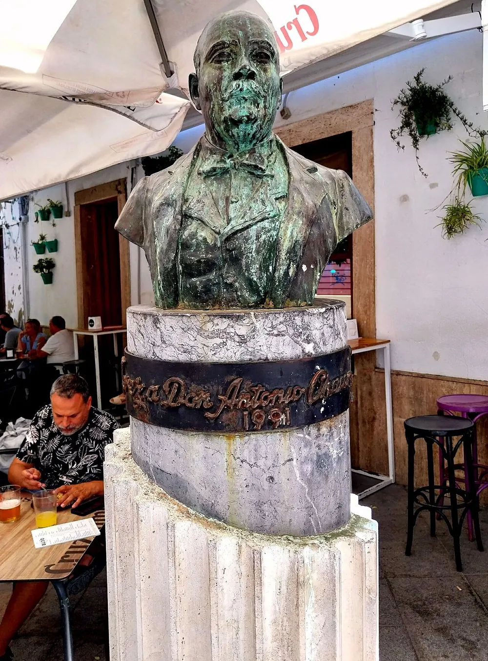 A green bronze bust of the singer Antonio Chacón on a stone plinth in Jerez, with café tables behind
