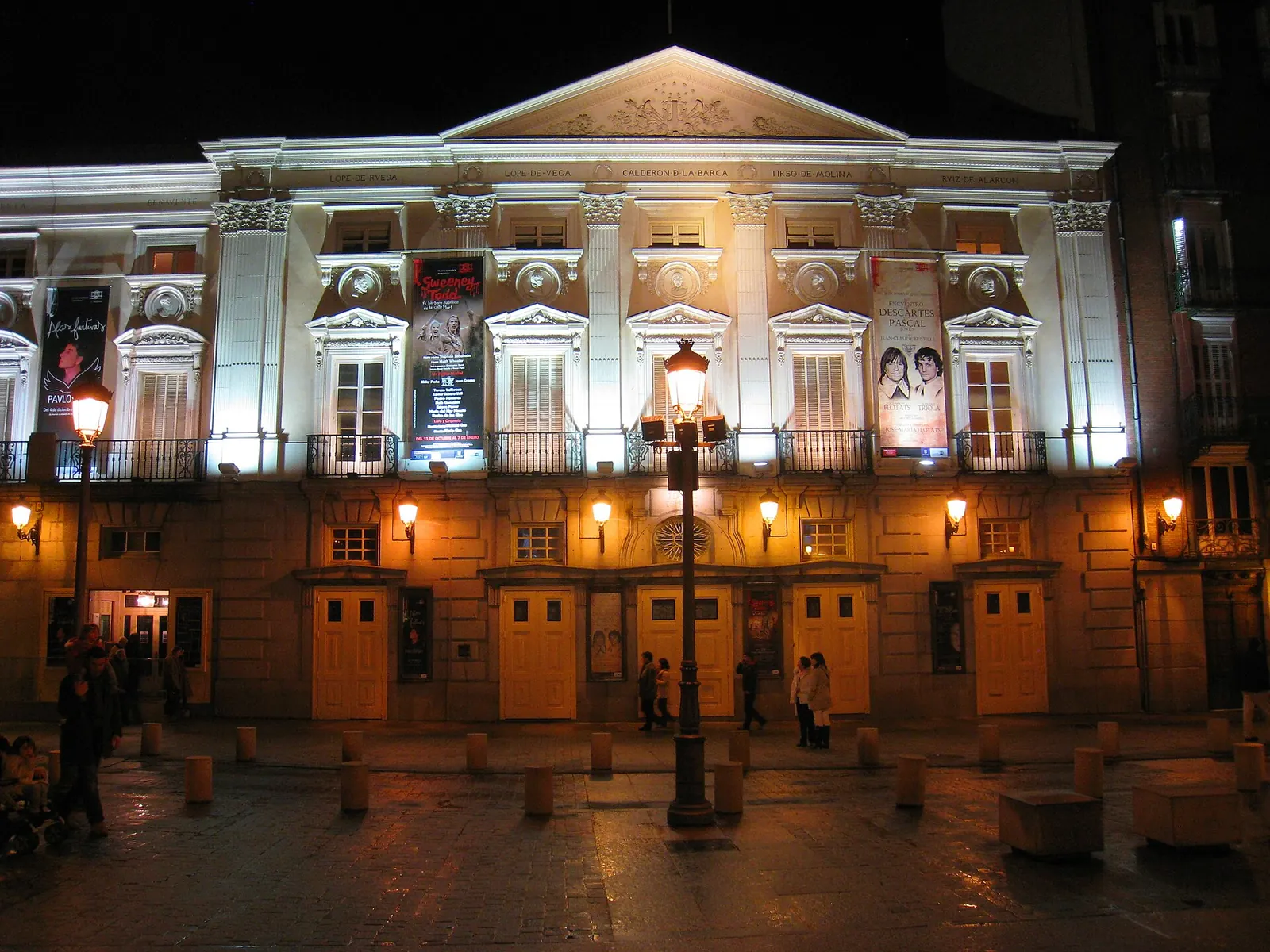The pale front of Teatro Español on Plaza de Santa Ana at night, lit by street lamps